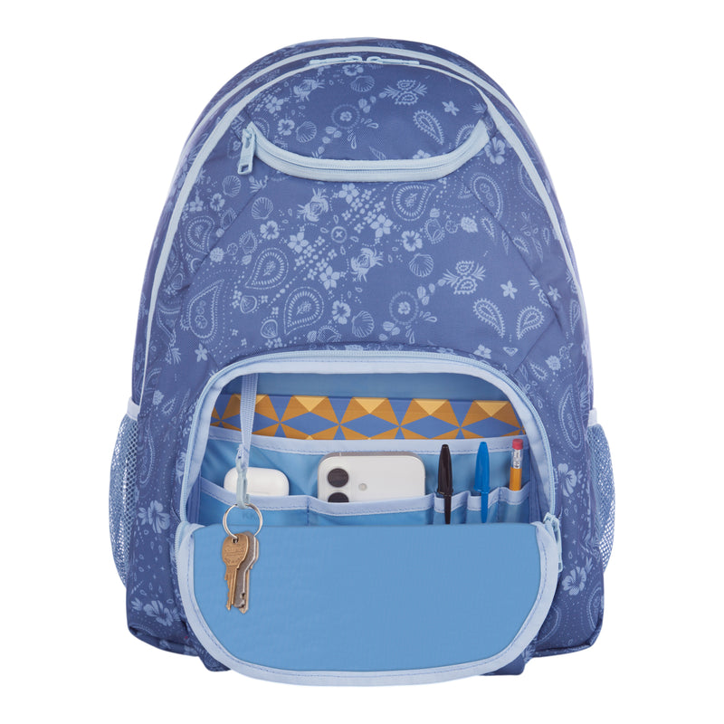 A Roxy Shadow Swell Backpack in blue with a floral pattern is shown with the front pocket unzipped, revealing keys, a phone, pens, pencils, and a yellow-patterned notebook inside.