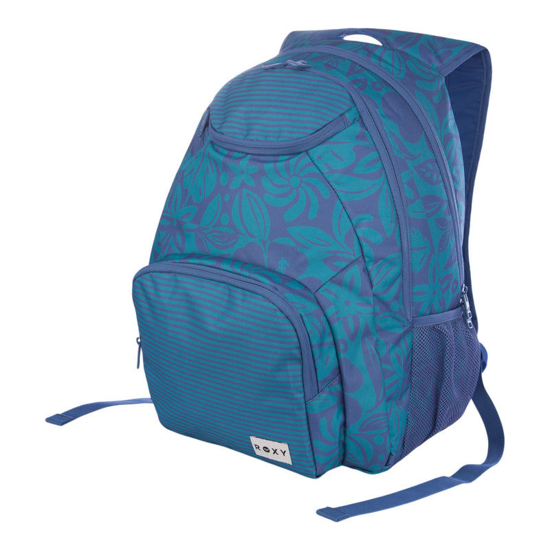 The Roxy Shadow Swell Backpack is a blue bag with a floral pattern, featuring a front pocket, side mesh pockets, and a top handle. The lower front pocket displays the Roxy brand label.