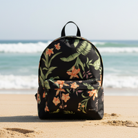 Floral-patterned backpack on a sandy beach with ocean waves in the background