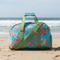 Floral patterned duffel bag on sandy beach with ocean in background
