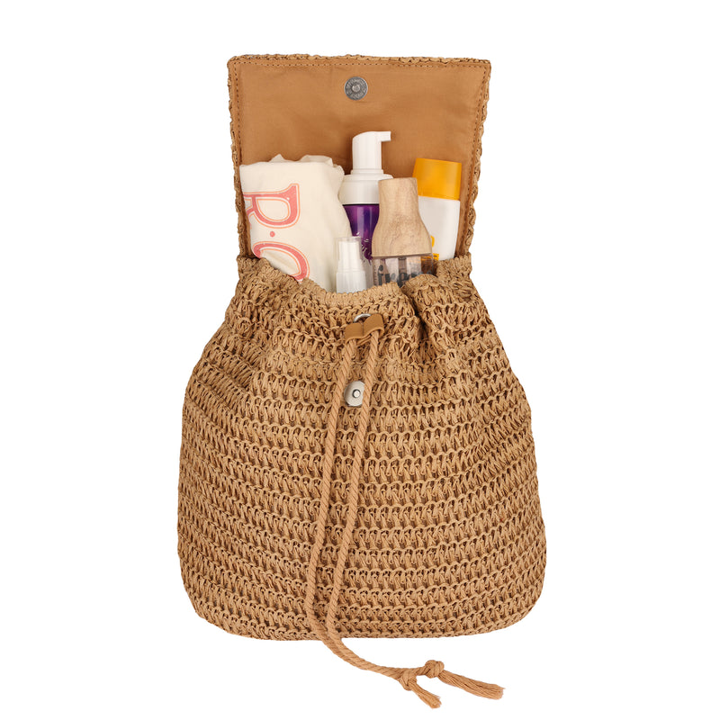 The Roxy Spotless Sunnies Backpack, a woven tan bag with a flapover closure and drawstring, sits open to reveal several personal care items inside, including bottles, tubes, and spray containers.