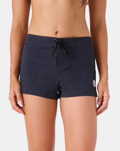 A woman wears the Roxy To Dye 2" Boardshort, featuring a drawstring waist and small circular logo on the left leg, against a white background. These stylish black swim shorts are perfect for versatile beachwear or as a comfortable cover-up.