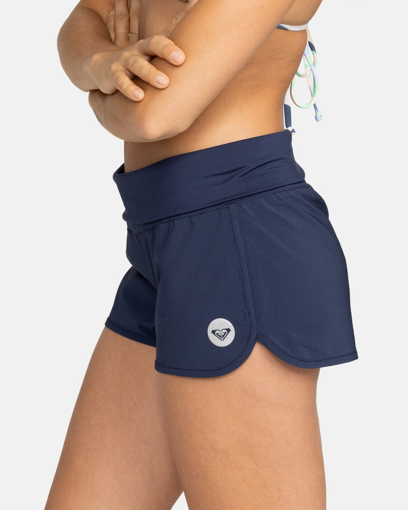 A person in a swimsuit top and Roxy Endless Summer Boardshort stands with arms crossed from shoulders to mid-thigh, against a plain white background.