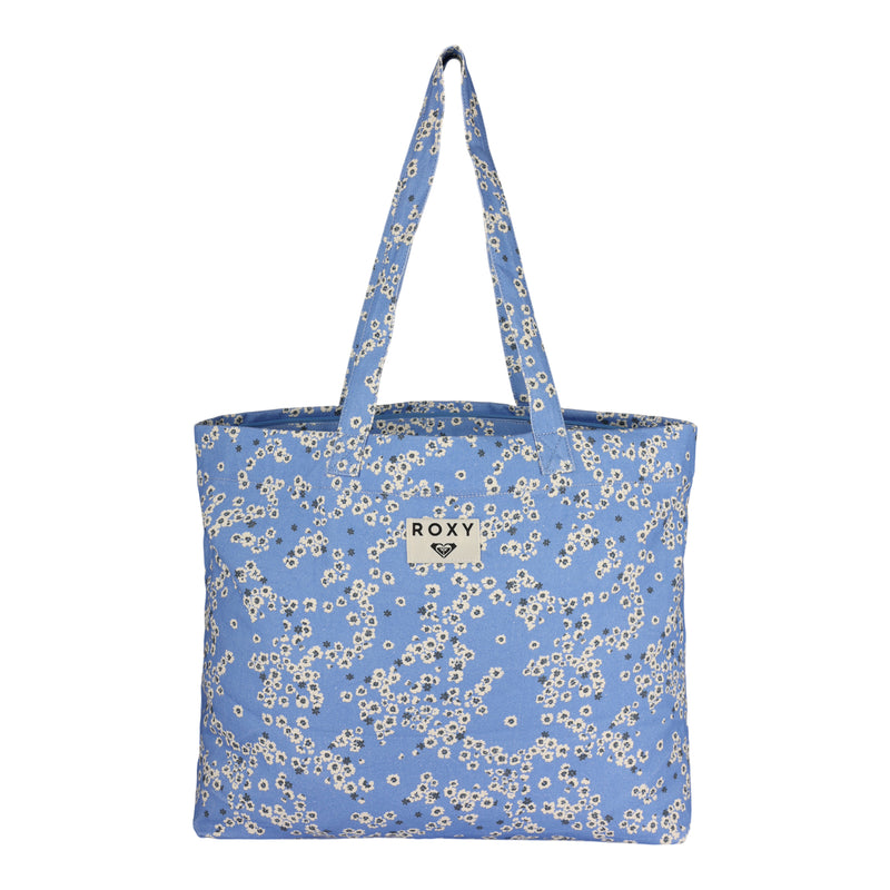 The ROXY Sweeter Than Honey Tote Bag features a blue design with a white floral pattern, two sturdy handles, and a rectangular ROXY logo label on the front center. This eco-friendly tote bag is showcased against a white background.