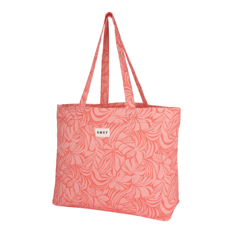 The ROXY Sweeter Than Honey Tote Bag is a pink recycled cotton bag featuring a swirling leaf pattern, two shoulder straps, and a small white patch with the ROXY logo on the front.