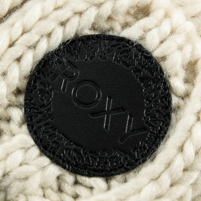 A close-up of a black circular leather patch with the Roxy logo embossed on it, sewn onto the cream-colored chunky cable knit Tram Beanie. This women’s beanie by Roxy features a cozy fleece-lined interior for added warmth and comfort.