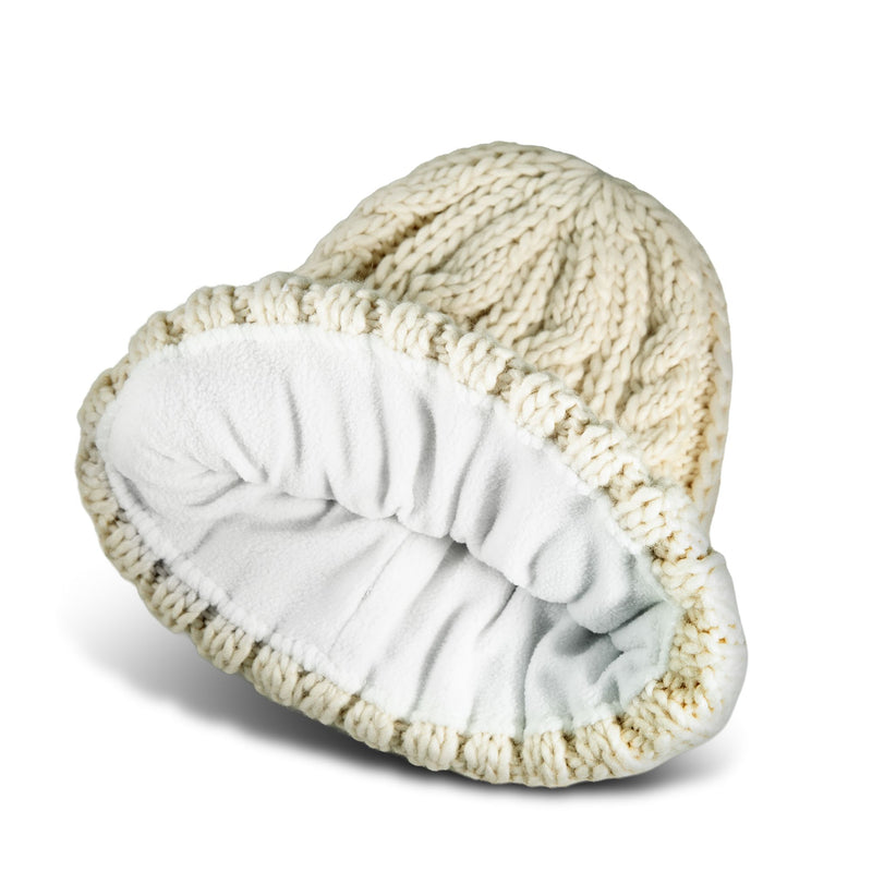 The Tram Beanie by Roxy is a cream-colored cable knit hat featuring a white, soft fleece lining, displayed here tipped over to reveal its cozy interior.