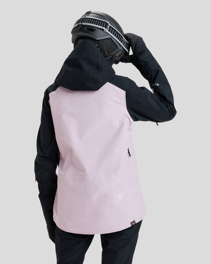 A person wearing a black helmet and gloves, with the Roxy Gore-Tex Lunalite Jacket in black and light pink, seen from behind against a plain gray background—perfectly outfitted for mountain performance.