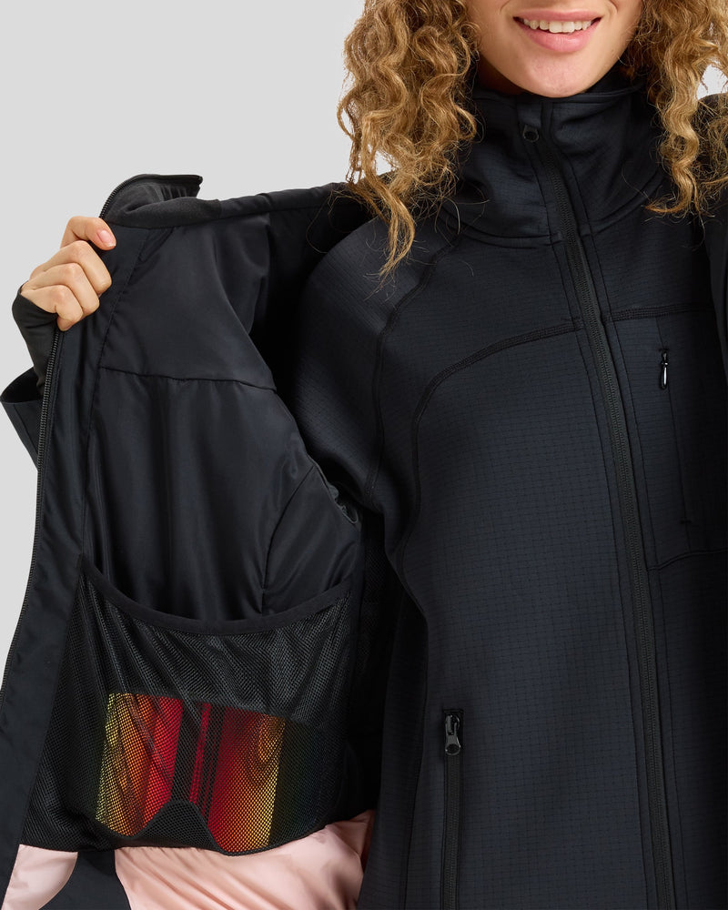A person wearing the Roxy Gore-Tex Stretch Purelines Jacket in black holds it open to reveal an inner mesh pocket containing ski goggles with red lenses. Only their curly hair and lower face are visible.