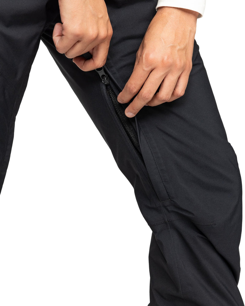 A person’s hands are unzipping a black zipper pocket on the side of Roxy Gore-Tex Spridle Pants while wearing a long-sleeve shirt.