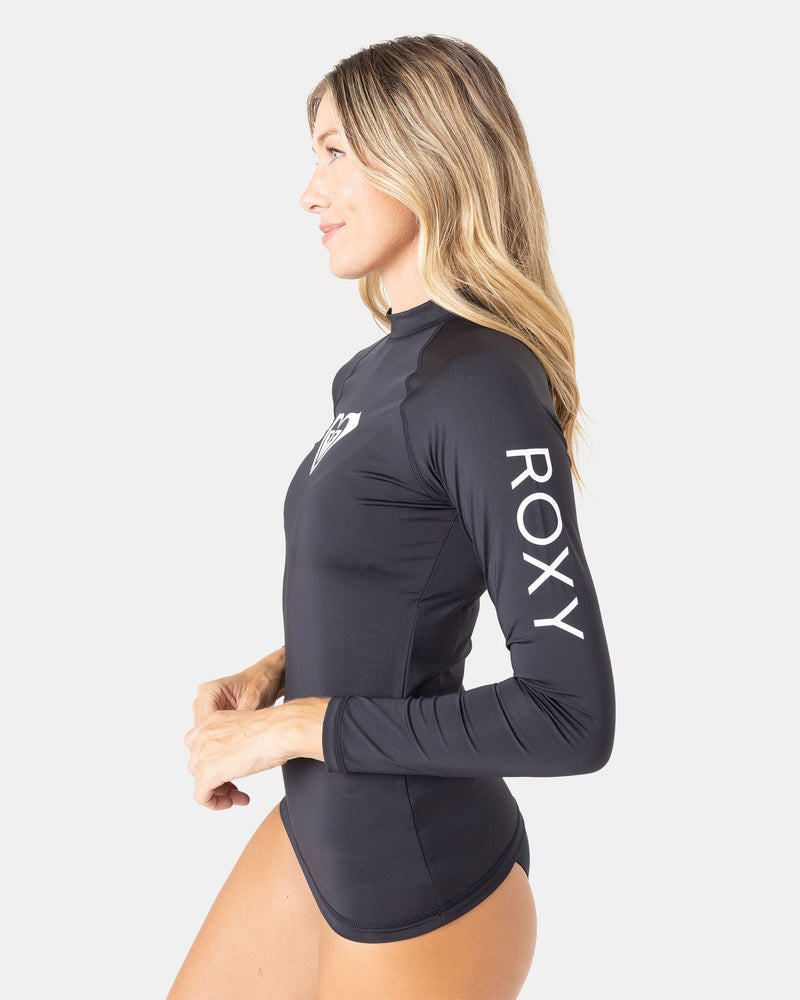 A woman in profile wears the Roxy Whole Hearted Ls Rashguard, a black long-sleeve top made from recycled stretch fabric, against a plain white background.
