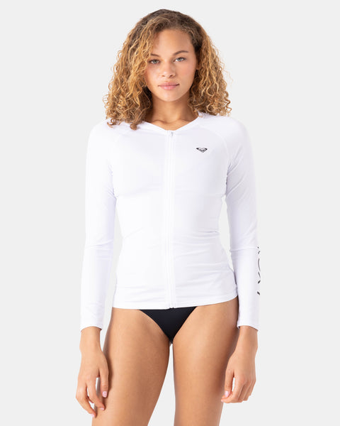 A woman with curly hair wears the Roxy New Essentials LS Zip Rashguard in Bright White with black bikini bottoms, standing against a plain light background.