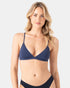 A woman with long, wavy blonde hair models the Roxy Sd Beach Classics Fixed Tri navy blue triangle bikini, made from recycled nylon. She stands against a light grey background, gazing at the camera with a neutral expression.