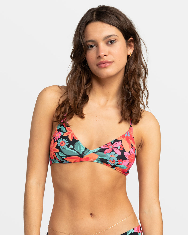 A woman wears a Roxy PT Beach Classics Strappy Bra Bikini Top in Anthracite The Palms, featuring a black strappy design with a pink, orange, and teal floral print.