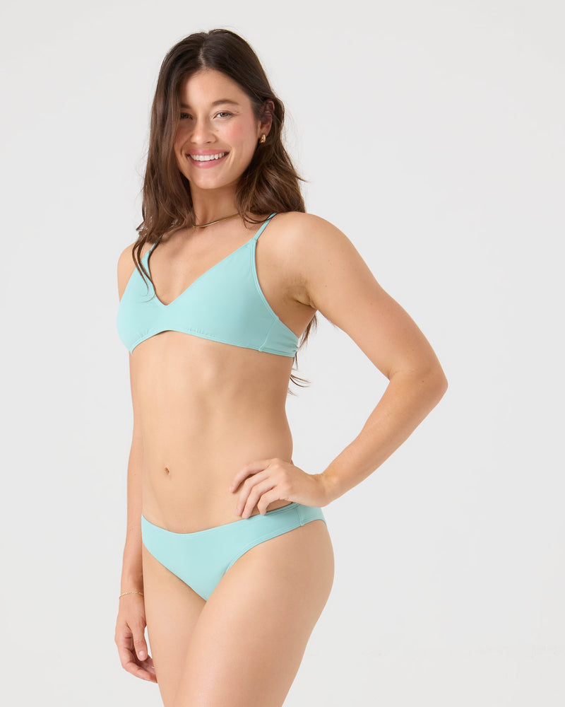 A woman with long brown hair poses with a smile and one hand on her hip, wearing the Roxy SD Beach Hipster Bottom Moderate Bikini Bottom against a plain white background.