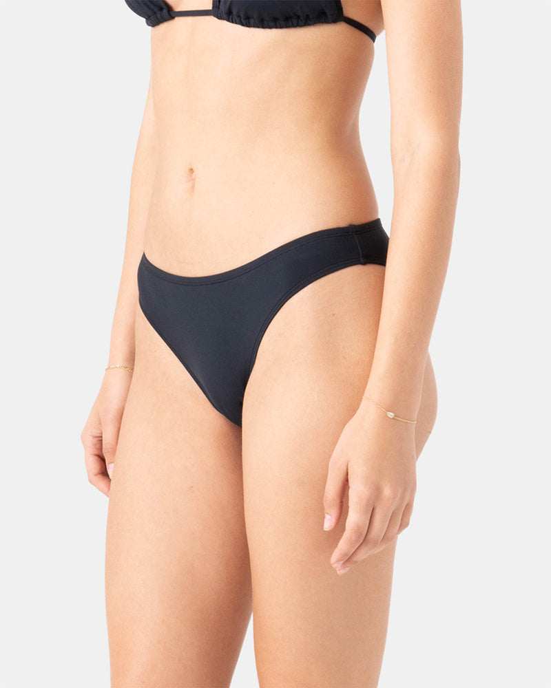 A woman wears the Roxy Sd Beach Classics Hipster Mod black bikini bottom, featuring a simple, minimalist design, shown from mid-torso to upper thighs against a plain light background.