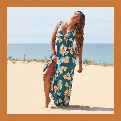 Woman in a floral dress standing on a sandy beach with ocean in the background