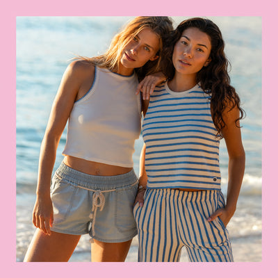 Two women standing on a beach, wearing matching sleeveless tops and shorts.