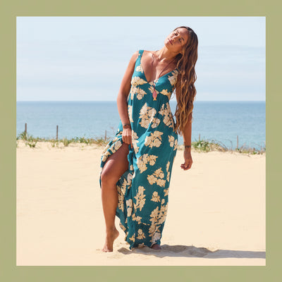Woman in a floral dress standing on a sandy beach with ocean in the background