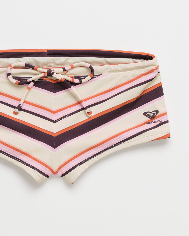 The ROXY x Madhappy Swim Short Cheeky Bikini Bottom features bold stripes in purple, orange, pink, and beige, with a drawstring waist and a subtle Madhappy logo on the right side. Displayed against a white background, this exclusive piece from the Roxy x Madhappy collection combines vibrant style with comfort—perfect for your next beach day.