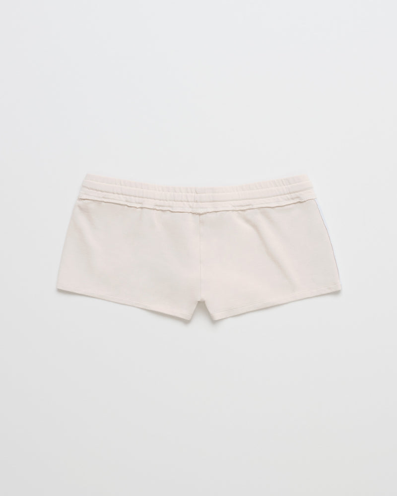 A pair of ROXY x Madhappy French Terry Mini Shorts in a soft Birch finish, featuring an elastic waistband, is displayed from the back against a plain white background.