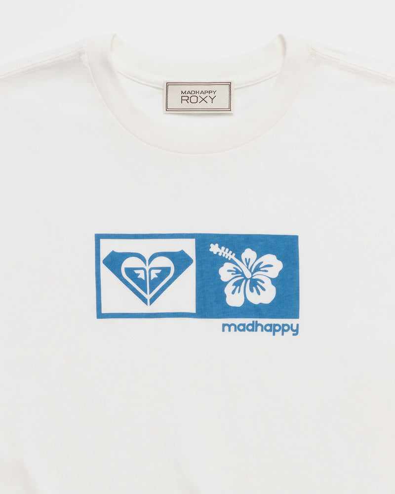Close-up of the ROXY x Madhappy Long Sleeve T-Shirt, a white top with a Roxy x Madhappy neck label. The front showcases a blue graphic box centered on the chest, featuring the Roxy heart logo alongside a white hibiscus flower and “madhappy” printed in blue below. This versatile piece is part of the exclusive Roxy x Madhappy collaboration.