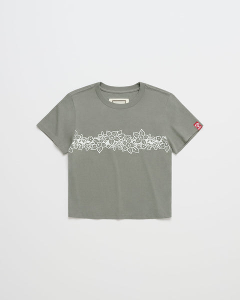 The ROXY x Madhappy Shrunken Tee by Roxy x Madhappy is a Kelp-colored, close-to-body staple short-sleeve T-shirt featuring a white floral pattern across the chest and a small red patch on the left sleeve. The shirt is shown laid flat on a white background.