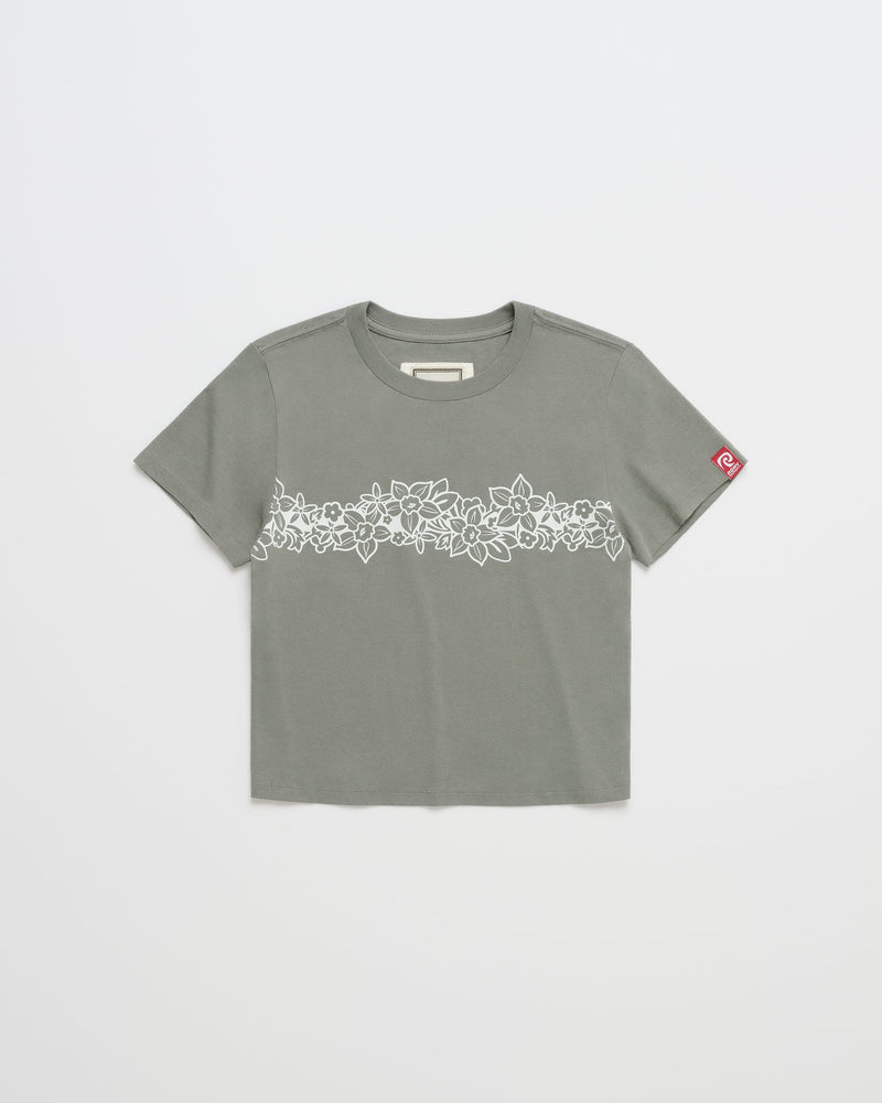 The ROXY x Madhappy Shrunken Tee by Roxy x Madhappy is a Kelp-colored, close-to-body staple short-sleeve T-shirt featuring a white floral pattern across the chest and a small red patch on the left sleeve. The shirt is shown laid flat on a white background.