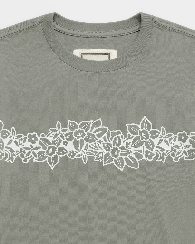 Introducing the ROXY x Madhappy Shrunken Tee—a kelp green t-shirt from Roxy x Madhappy, featuring a close-to-body fit and a striking white floral design in a horizontal band across the chest, adorned with various flowers and leaves. Perfect for giving your everyday wardrobe a fresh update.