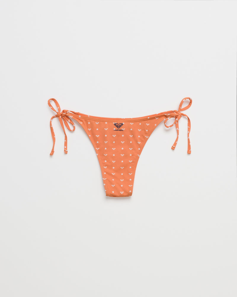 ROXY x Madhappy Tie Side Cheeky Bikini Bottom, featuring a small white heart pattern in the Apricot Spice colorway, shown flat on a white background—a playful swim style from the Roxy x Madhappy collaboration.