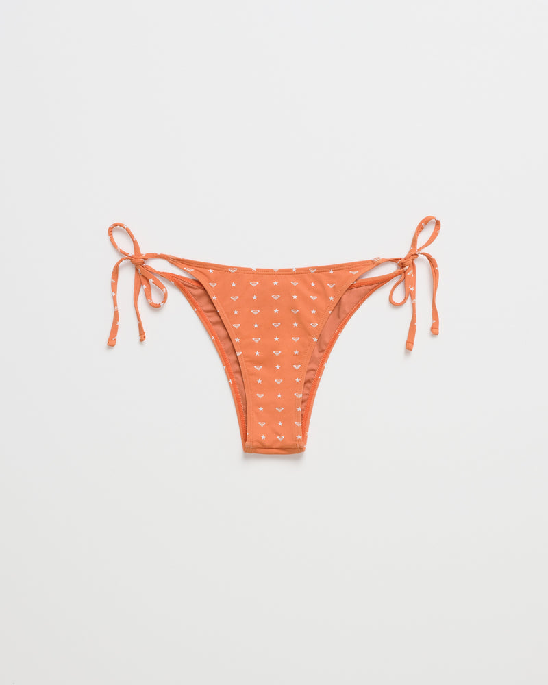 ROXY x Madhappy Tie Side Cheeky Bikini Bottom by Roxy x Madhappy in orange with small white heart patterns, featuring adjustable tie sides and a cheeky cut, displayed flat on a plain white background.