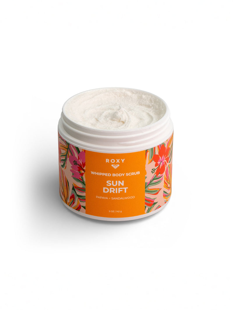 A white jar of Roxy’s Sun Drift Body Scrub features a bright orange label with tropical florals and notes of papaya and sandalwood; the open lid reveals creamy exfoliation inside.