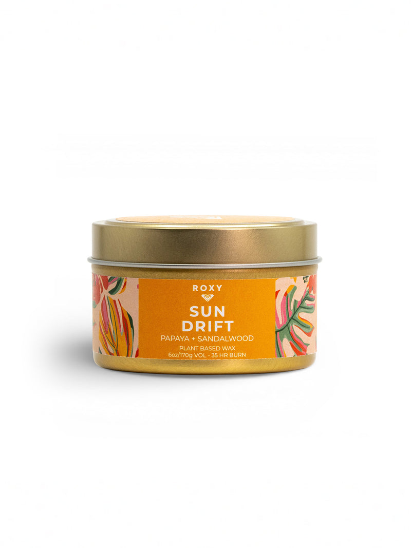 The Roxy Sun Drift Palm Tin Candle features a tropical papaya and sandalwood scent in a small gold tin. Its orange floral label highlights plant-based wax and a long-lasting 45-hour burn time.