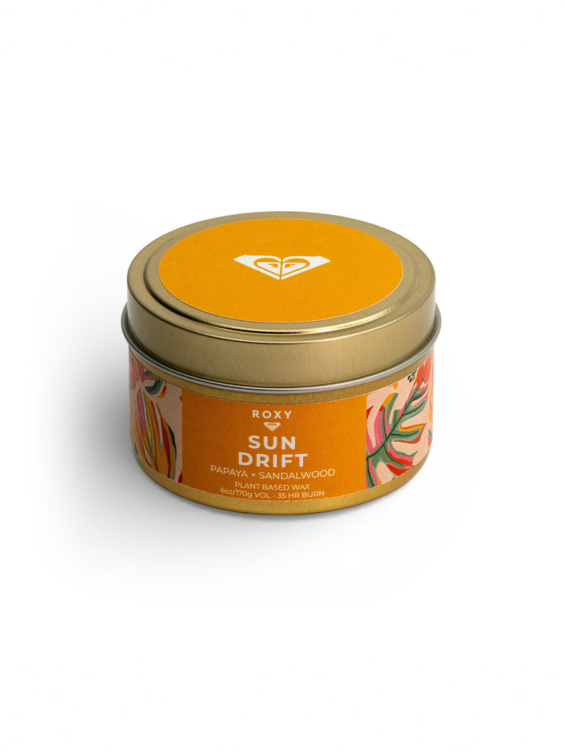 The Roxy Sun Drift Palm Tin Candle features a round tin with a gold lid, orange label, and abstract floral design. Enjoy a tropical papaya and sandalwood scent from plant-based wax, with up to 45 hours of burn time.