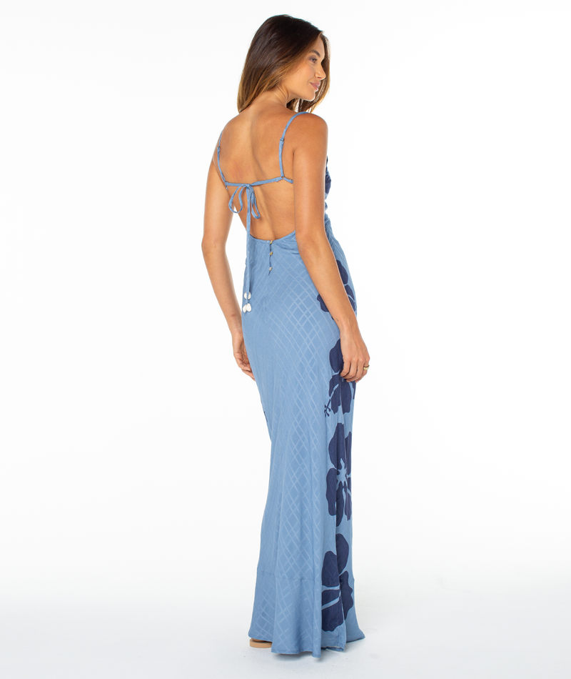 A woman seen from behind wears a floor-length, blue patterned Roxy Lush Oasis Dress with a low, tie-back closure.
