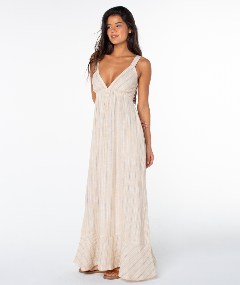 A woman models the Roxy Wilder Coast Dress, a sleeveless, light beige floral print maxi with a deep V-neck and subtle vertical stripes, standing against a plain white background.
