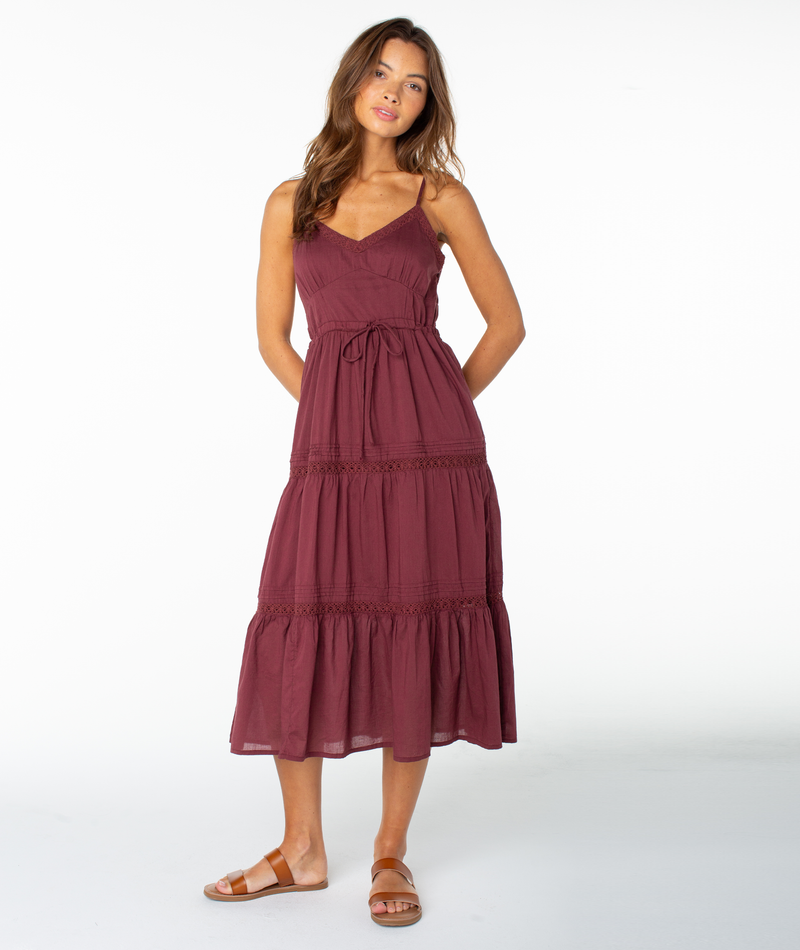 A woman wearing the sleeveless, ankle-length Roxy Azalea Dress in Port Solid with spaghetti straps and brown sandals stands against a plain white background—a versatile transitional piece for effortless style.