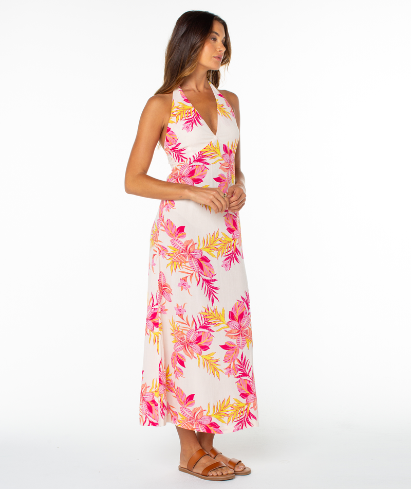 A woman stands against a white background wearing the Roxy Beach Day Maxi Dress with pink and yellow florals, sleeveless halter neckline, and brown sandals.