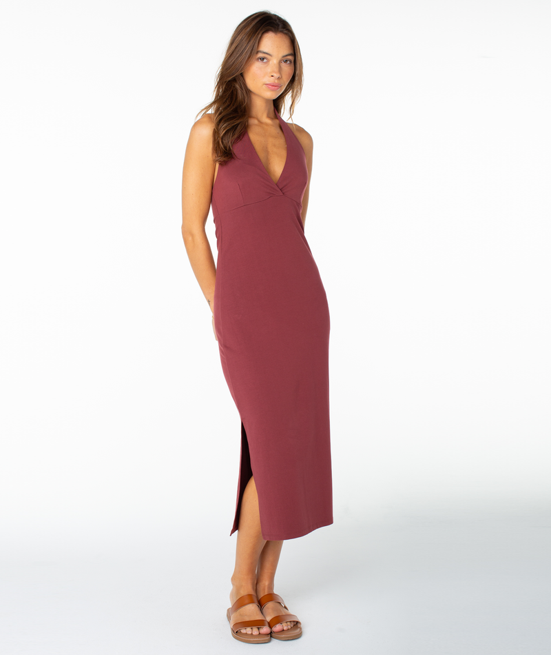 A woman stands against a plain white background wearing the Roxy South Shore Midi Dress—an effortless off-duty, sleeveless burgundy dress featuring a V-neckline and side slit—paired with brown sandals.