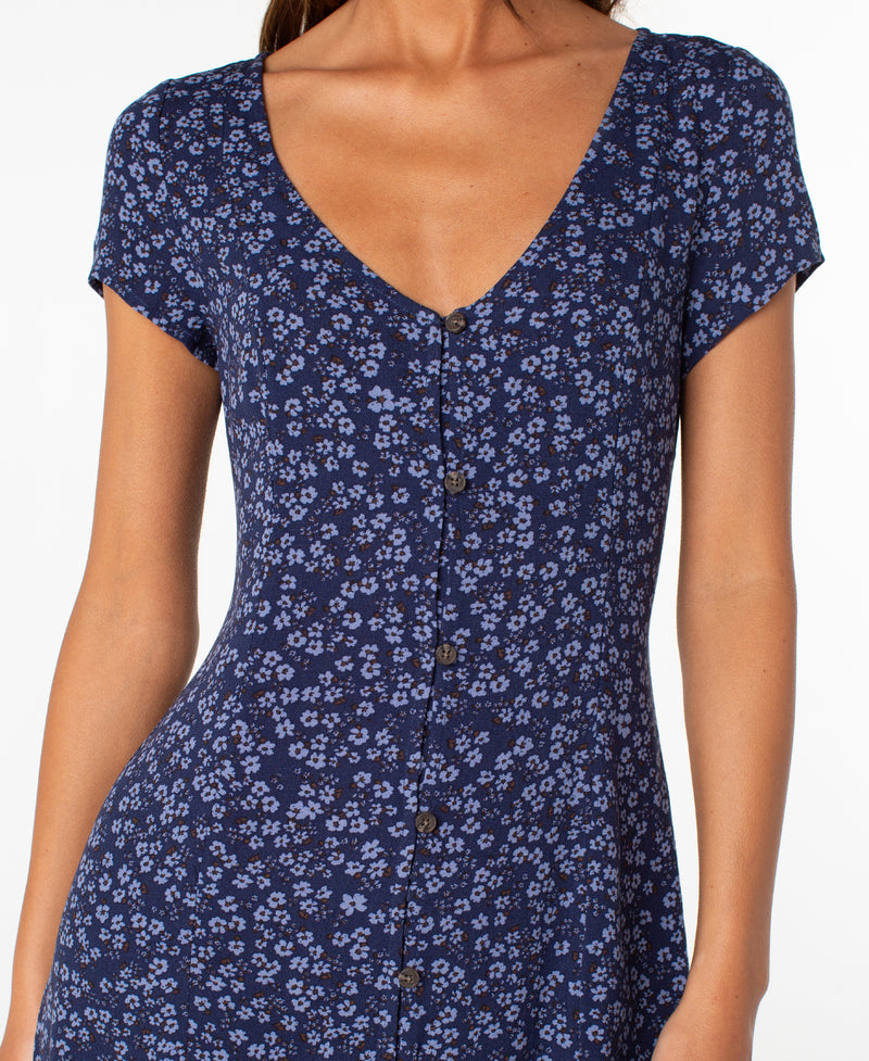 A woman is shown from shoulders to mid-thigh against a white background, wearing the Roxy Cool Breeze Mini Dress—a short-sleeve, deep V-neck navy dress featuring small blue floral patterns and buttons down the front, perfect for any occasion.