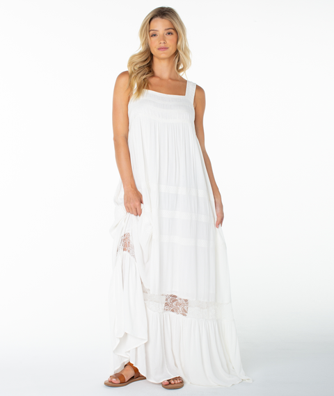 A woman with long blonde hair wears the Roxy Summer Wind Maxi Dress in Coconut Milk Solid—a flowing white dress with lace detail and a square neckline—paired with brown sandals, posed against a plain white background.