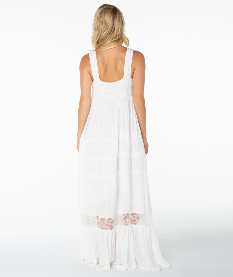 A woman with blonde hair faces away, wearing the Roxy Summer Wind Maxi Dress—a long, sleeveless white dress with a square neckline and lace detail near the hem—against a plain white background.