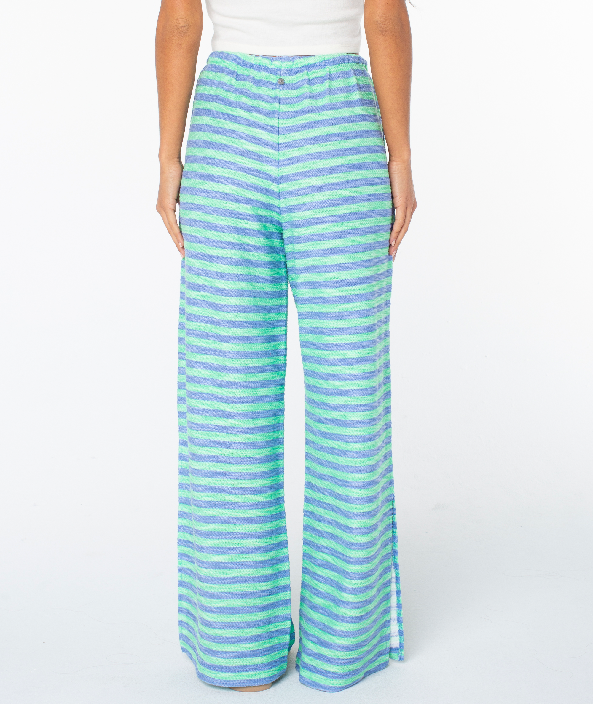 A person is shown from the back wearing Roxy’s Beach Breeze Pant—high-waisted, wide-leg pants with blue and green horizontal stripes, an elastic waistband, and paired with a sleeveless white top.