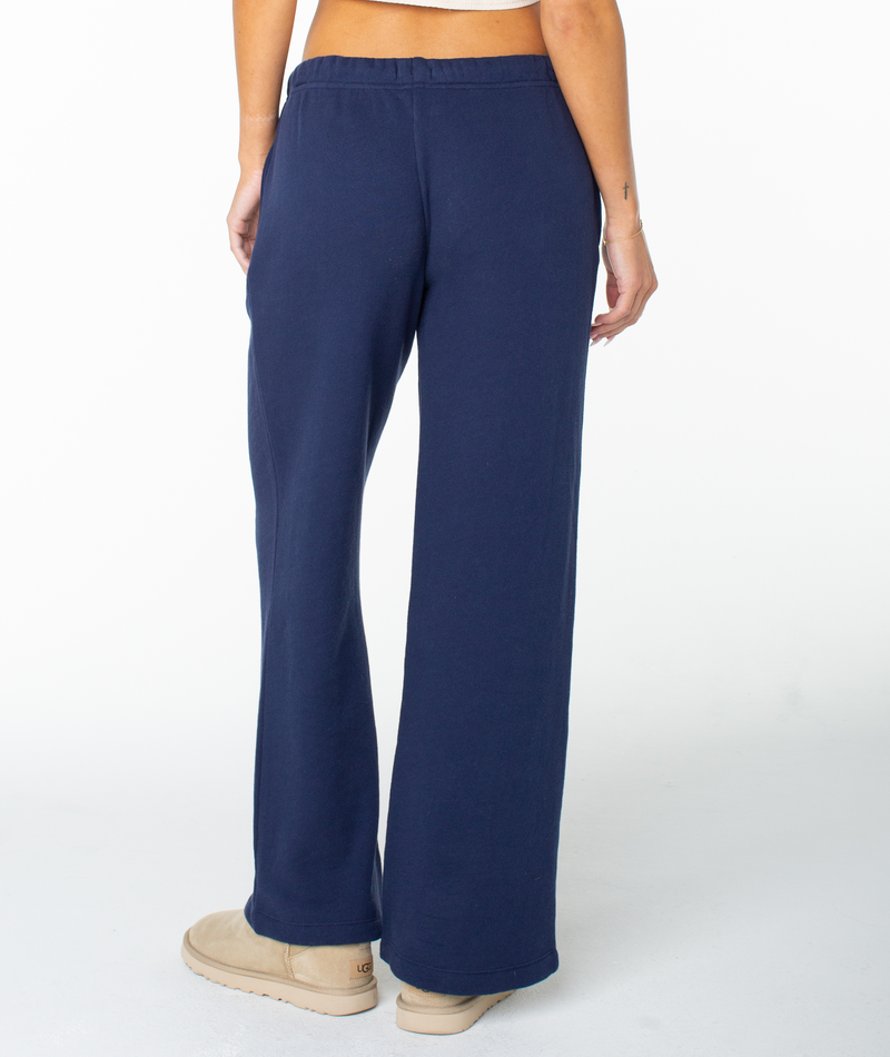 A person wearing navy blue Roxy Good Times Pant sweats and beige slippers stands facing away, displaying the back of the pants against a plain white background.