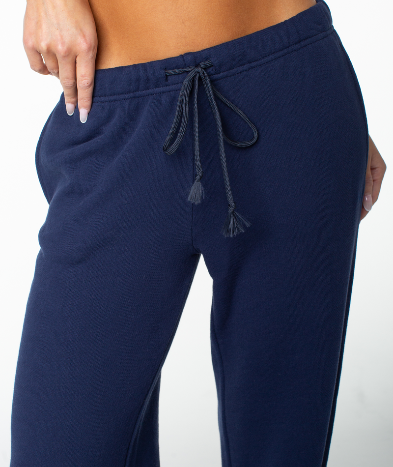 Someone wears navy blue Roxy Good Times Pant drawstring sweats, their hand tucked in a pocket, shown from the waist down against a plain backdrop—ideal to pair with the matching Dream Thing top.