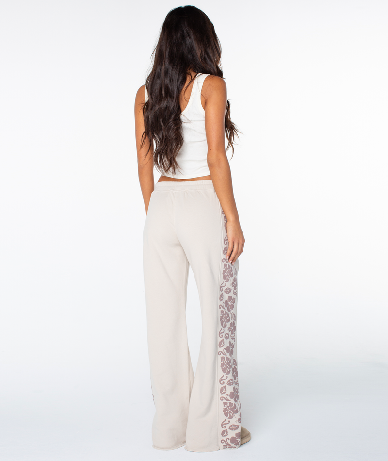 Woman with long brown hair stands facing away in a white tank top and Roxy Fringing Reefs Pant, featuring beige fabric with leopard print side panels, against a plain white background.