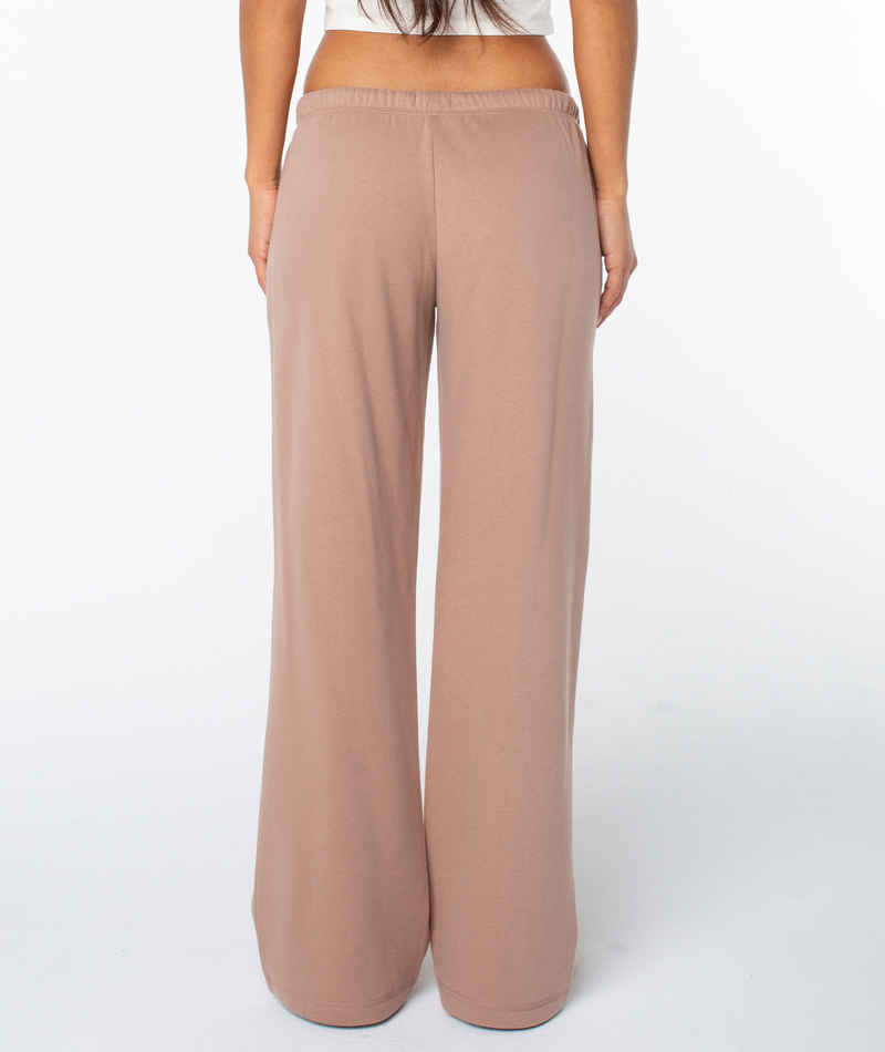 A person stands facing away against a white background, wearing Roxy’s Ariel Wide Leg Pant in beige with a white top.