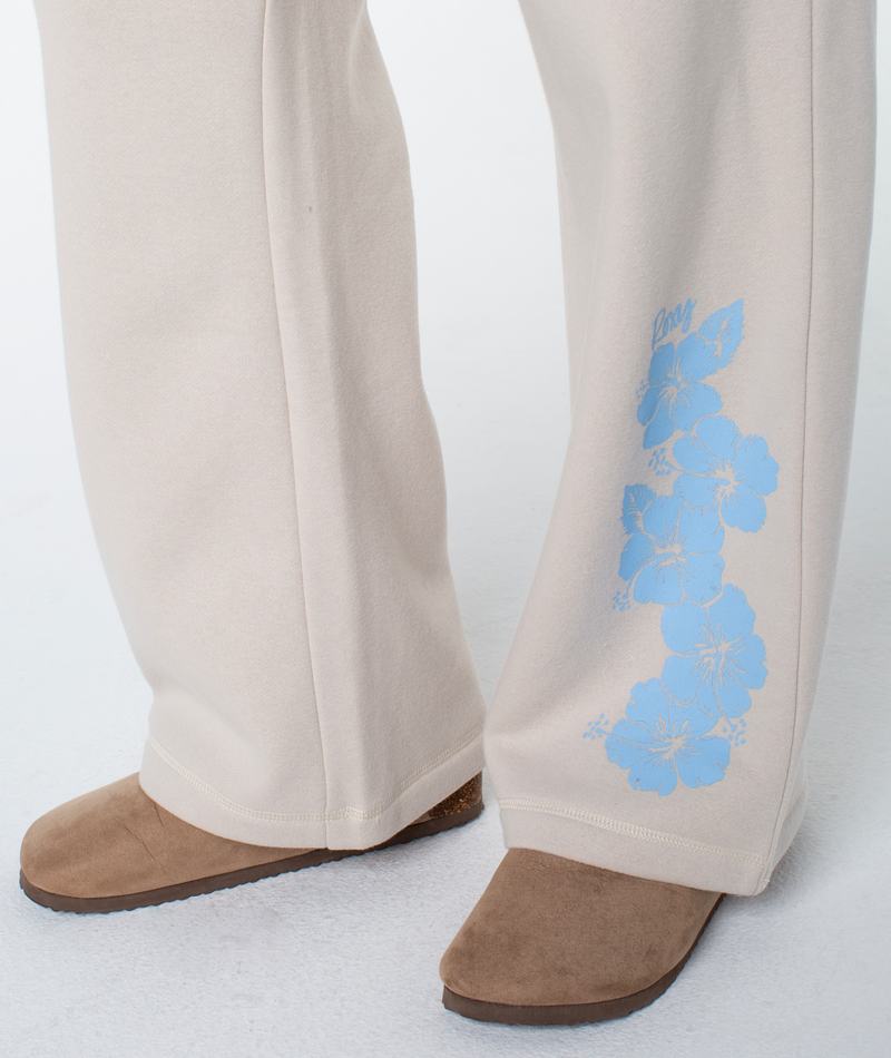 Person wearing the Ariel Wide Leg Pant by Roxy, featuring a beige color and blue floral print near the cuff, paired with brown suede shoes—ideal for beachside lounging.