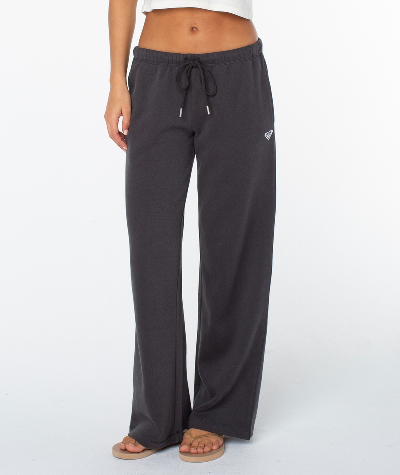 Model wears Roxy’s Ariel Wide Leg Pant—loose-fitting sweatpants in a soft cotton blend—with a white cropped top and sandals, shown from the waist down against a plain white background.