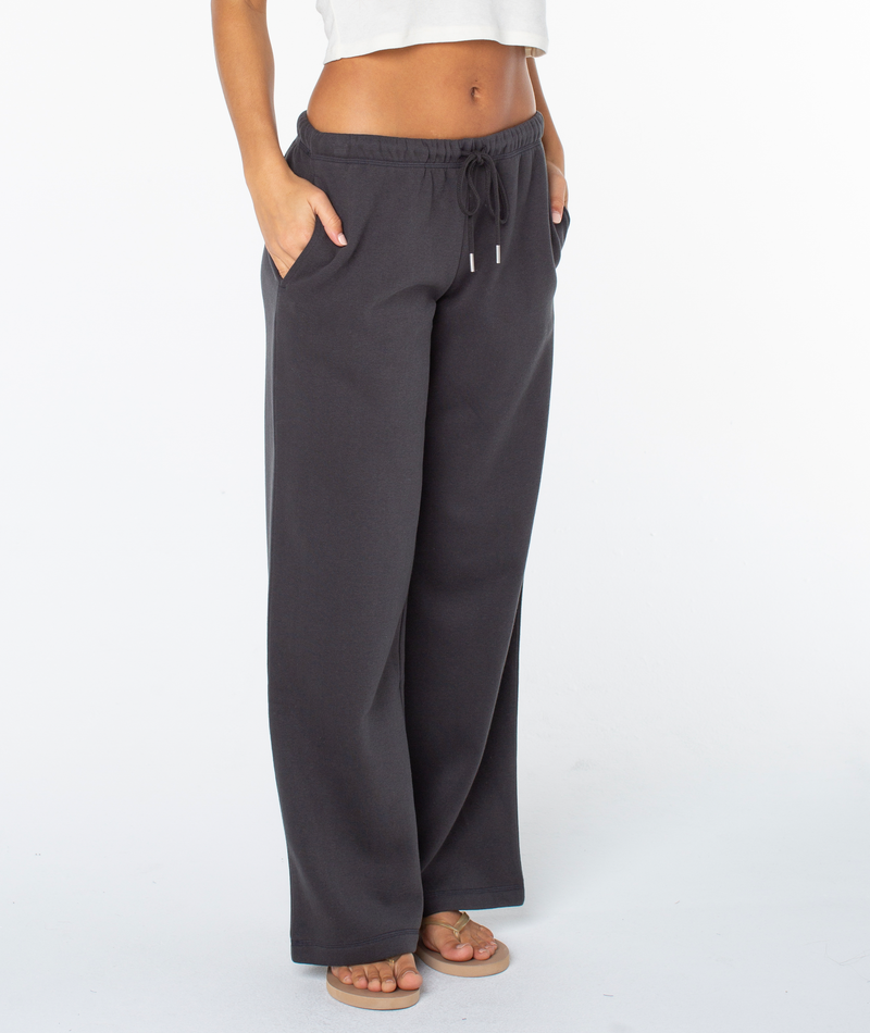 A person models the Roxy Ariel Wide Leg Pant with a white crop top and sandals, standing hands-in-pockets against a plain white background.